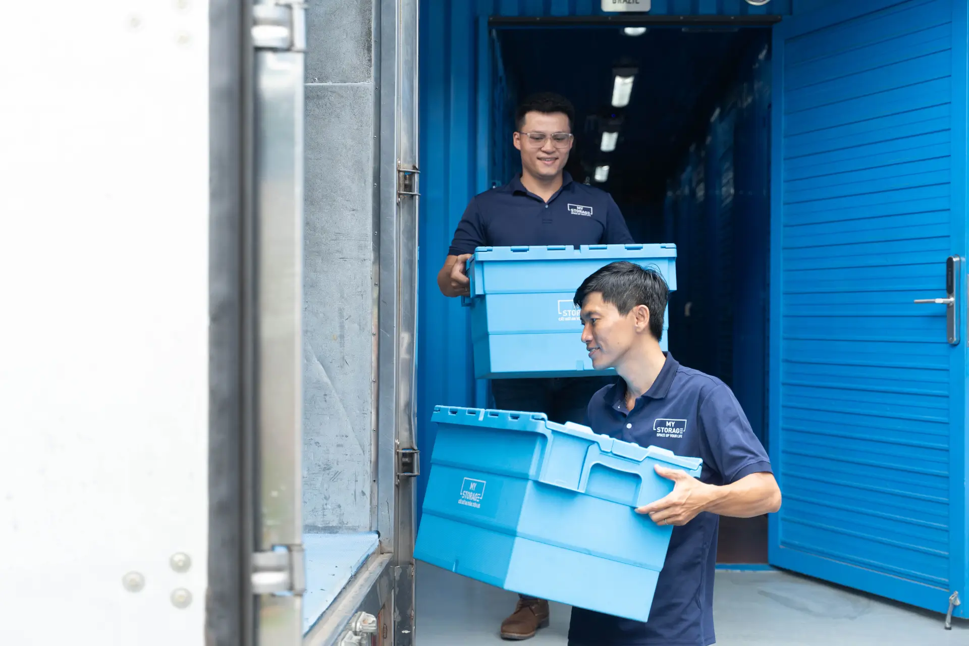 Mover carrying a blue storage container into a MyStorage warehouse.