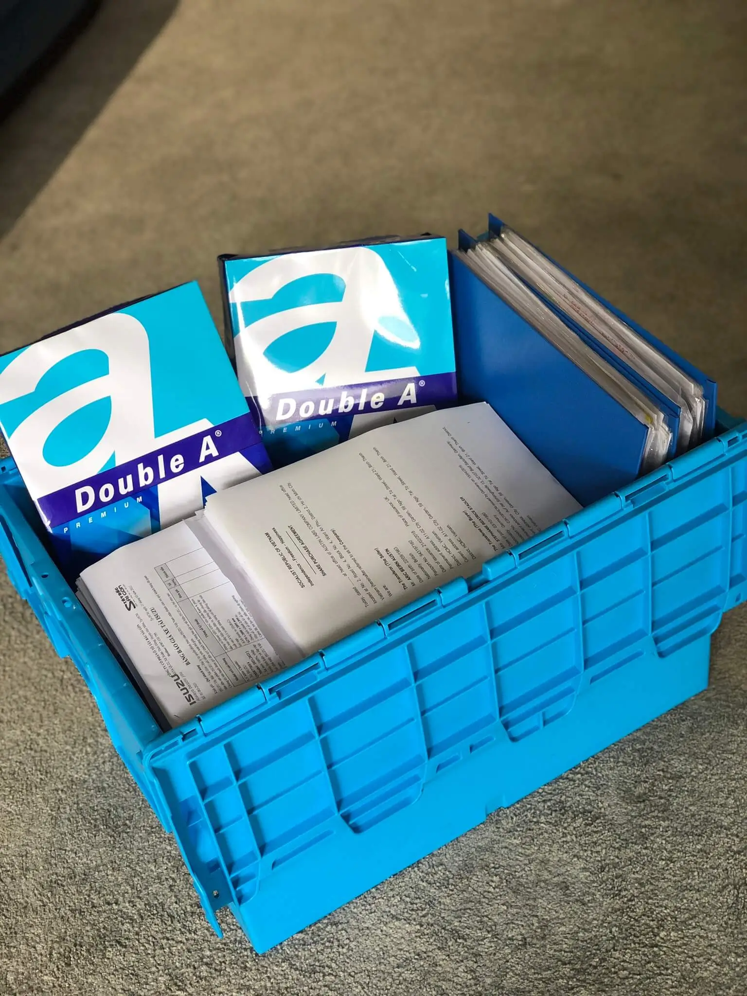 Blue plastic storage crate filled with paper reams and folders