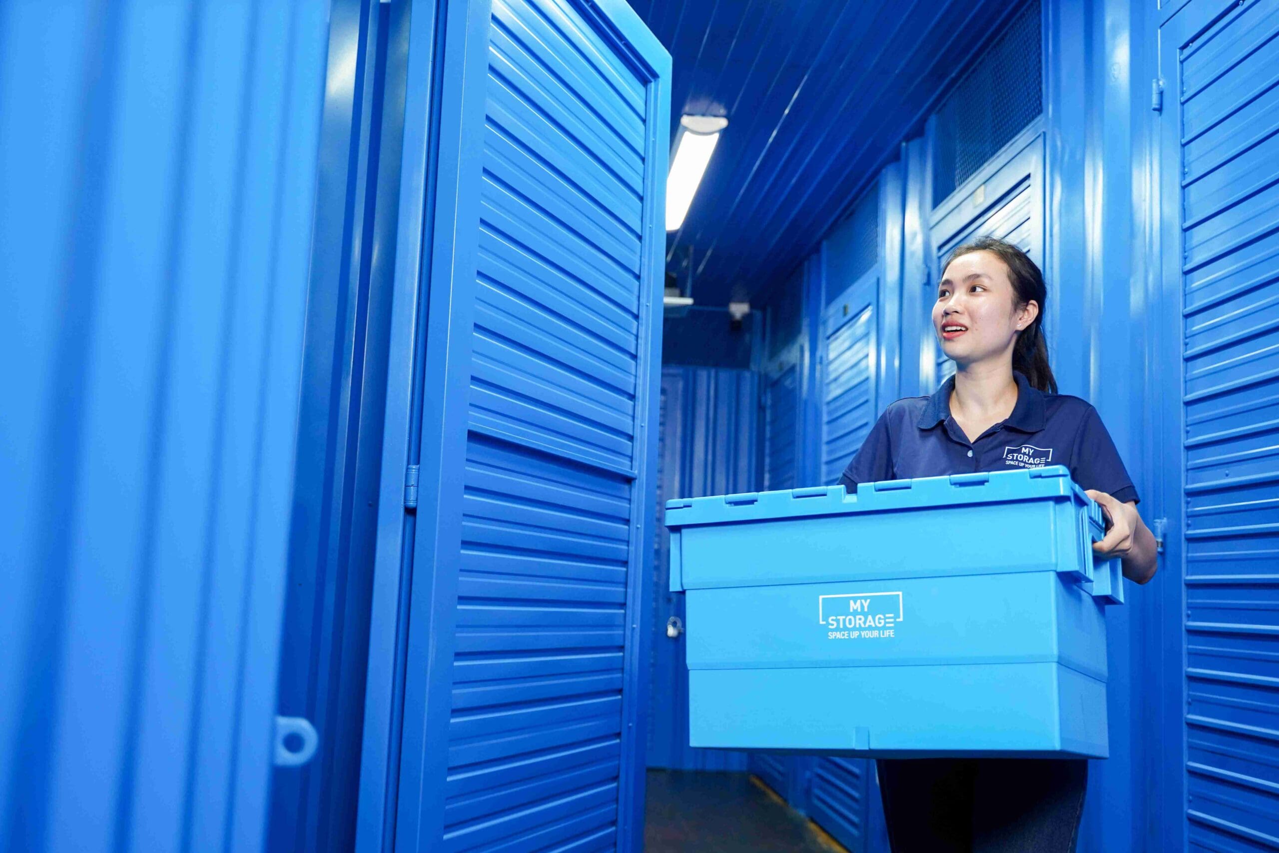MyStorage staff member carrying a blue storage box down a locker corridor